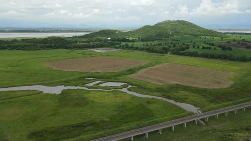 Descending aerial footage revealing hills from a distance, lake, farmlands; Elevated railways with a
