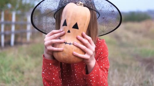Little Girl Witch Holds a Decorative Pumpkin