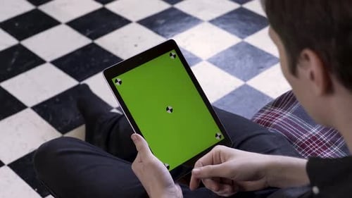 Man Using Tablet with Green Screen on Checkered Floor
