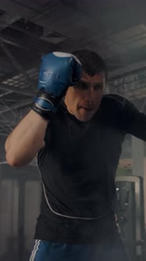 Muscular Man Powerfully Punches Heavy Bag in Gym