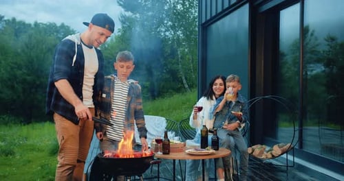 Family man woman and children which cooking sausages and vegetables on grill for barbecue party