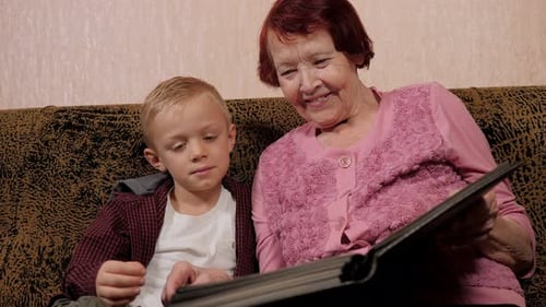 Una bisabuela feliz y un nieto pequeño miran un álbum de fotos grande