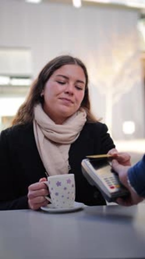 Young Woman Enjoying a Warm Cup of Coffee at an Outdoor Cafe While Preparing to Make a Payment with