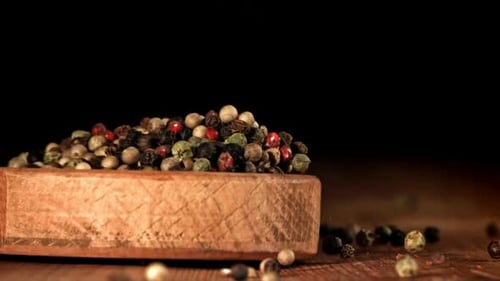 Multi-Colored Pepper falling from wooden bowl onto table