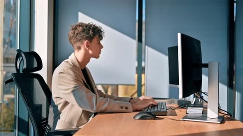 Young man is working in a computer in an office, windows on the background