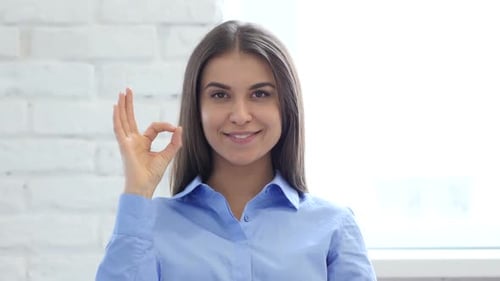 Young Woman Makes OK Sign, Smiles