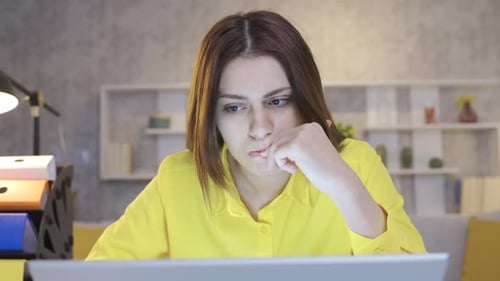 Pensive and confused young woman sitting in home office working on laptop worried.