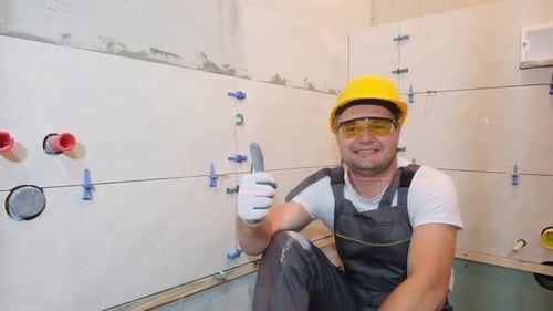Construction Worker Sitting on Floor and Showing Thumb Up and Smiling Looking at Camera