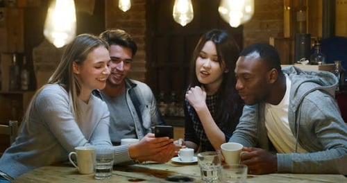 Slow motion of smiling friends having coffee at cafe and having fun with mobile cell phone. Shot i