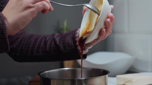 Woman Pouring Brown Liquid into Pot in Kitchen