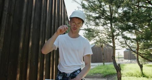 Young Architect or Builder with a Blueprint in His Hands Standing Outdoors on a Large Rural Building