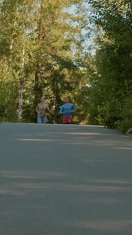 Young Man and Woman Sportswear Jogging Together in Forest on Chill Summer Day