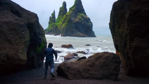 Man Running Through Boulders At Reynisfjara Black Sand Beach In Iceland With View Of Reynisdrangar