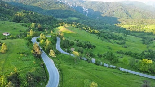 A Road Passes Hills Covered with Spruce Forests and Meadows Against a Cloudy Sky