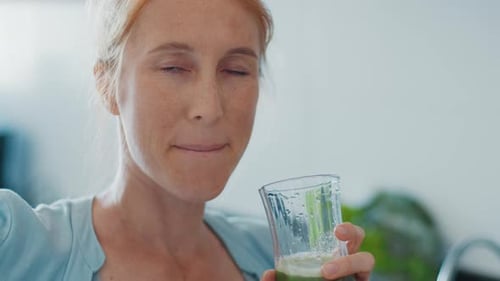 Healthy drink. Redhead woman drinks healthy green cocktail on the modern kitchen