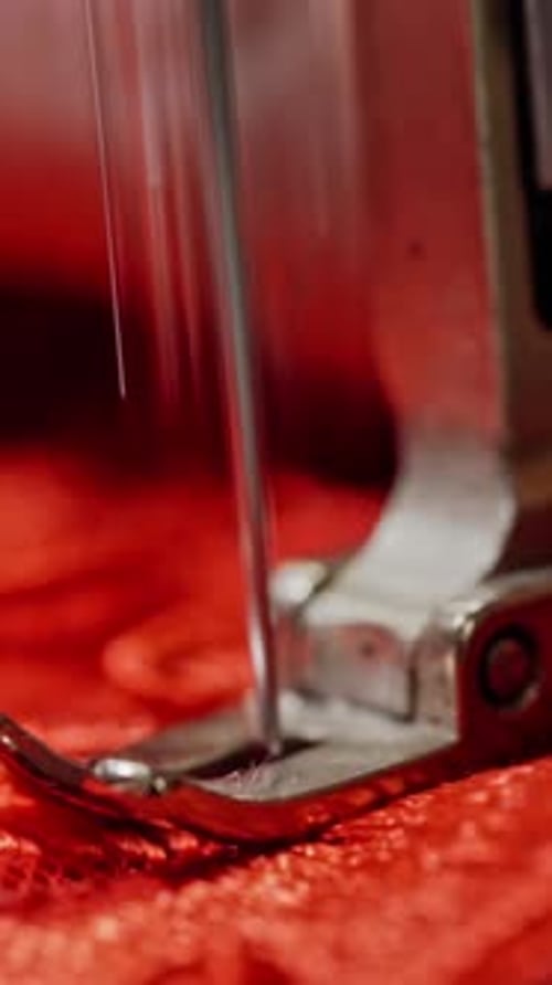 Steel part of sewing machine with a needle working on red cloth.