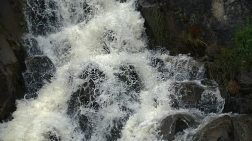 Detailed close-up of foamy waterfall water crashing over rugged rocks, emphasizing strength and