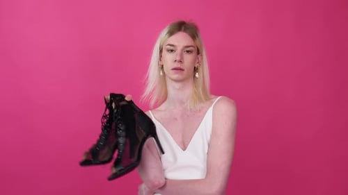 Transvestite Man with Shoes Against Pink Background