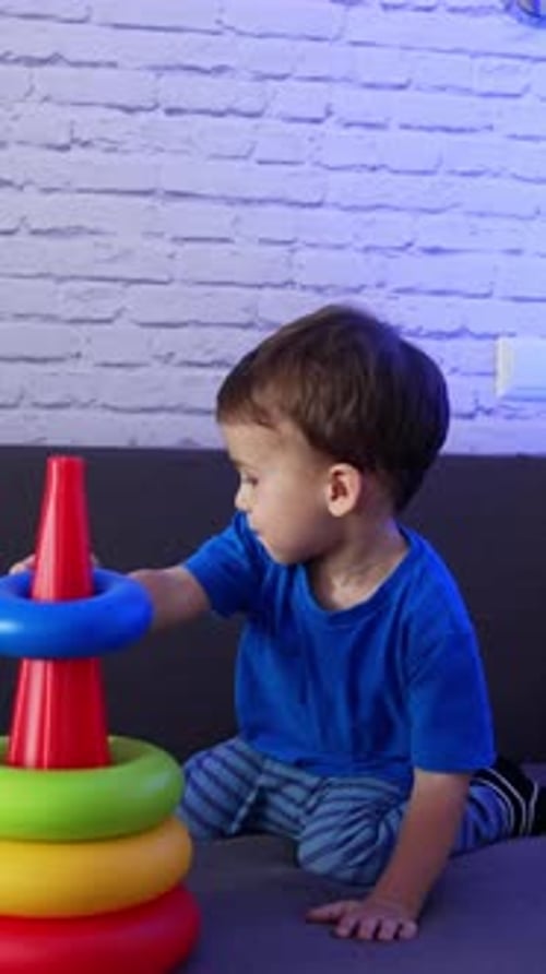 Hermoso bebé caucásico sentado en el sofá. Niño pequeño jugando con una pirámide de juguete.
