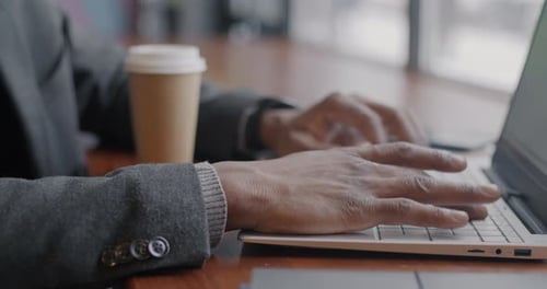 Closeup of Male Hands Typing with Laptop Computer While Businessman Working in Cafe and Drinking