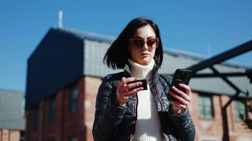 Frustrated Woman Using Mobile Gadget with Card in Hand While Standing on Street