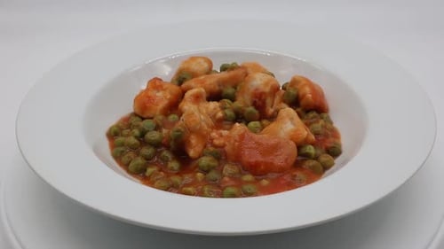 Turkey stew with green peas in a white dish rotating