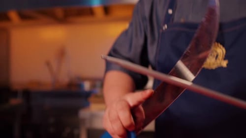 Close up of man butcher sharpens knife on professional sharpener.