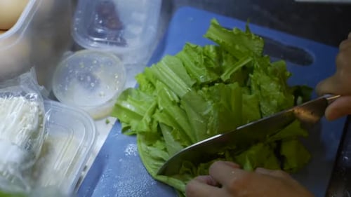 Green leaf vegetables being chopped into large pieces on blue chopping board, filmed as close up slo