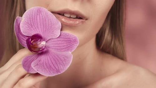 Woman Smiles Holding Orchid Flower Near Her Face