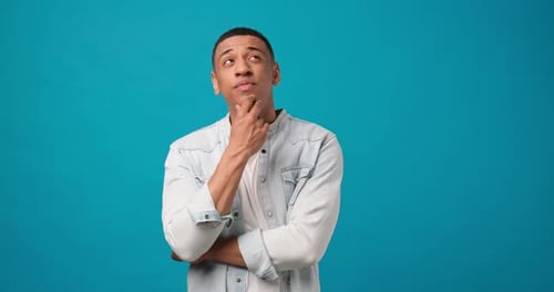 Young African American Man Thinking Ponder and Doubt Standing Over Blue Studio Background
