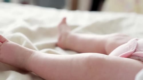 Primer plano de los alegres pies de un bebé recién nacido jugando en sábanas, con la mano, día