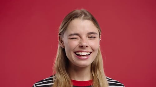 Smiling blonde woman winks on red background