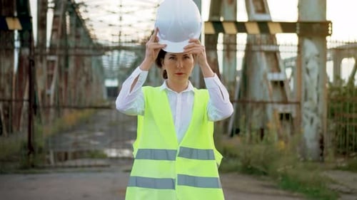 Woman Puts on Hardhat Near Old Steel Bridge