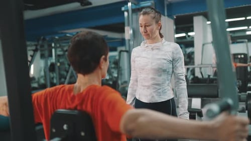 Man Works Out on Machine with Instructor Present