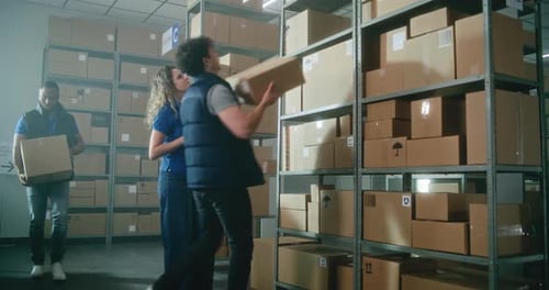 Male Warehouse Associate Puts Cardboard Box on the Shelf Female Inventory Manager Uses Tablet