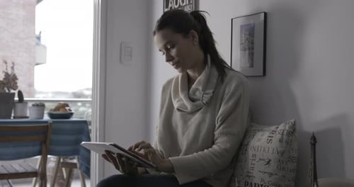 Mujer joven sentada en casa usando un ipad.