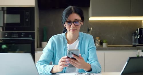 Woman with glasses working on phone in her hand messaging on smartphone in modern home office