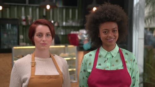 Portrait of two diverse young employees wearing aprons standing inside coffee shop. Young women