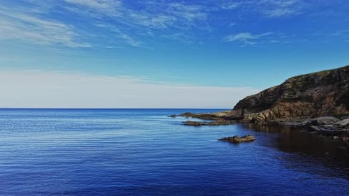 Coastal view of calm waters meeting rocky shoreline under blue skies