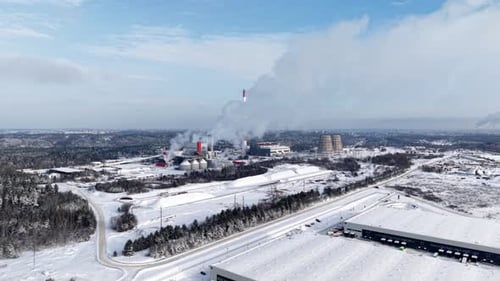 Wide drone panorama of a snowy highway and distant cogeneration facility releasing steam over