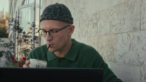 Junger Mann trinkt Kaffee, während er den Laptop im Freien benutzt