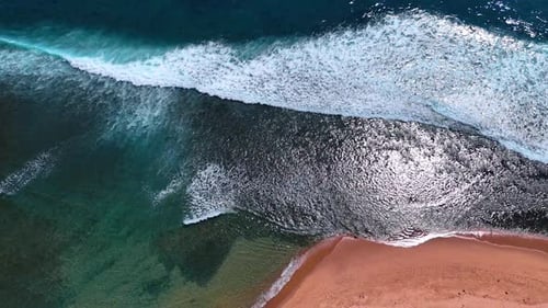 Beautiful foamy waves roll slowly to the sandy beach. Water of the ocean sparkles in the sun.