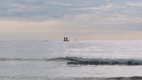 Figures on Distant Boat in Calm Sunrise Ocean