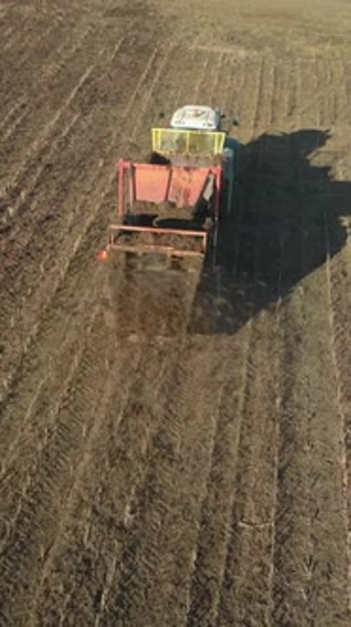 Vue de dessus verticale d'un tracteur avec un épandeur fertilisant un champ agricole