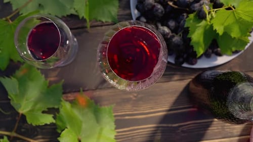 Rotwein in Kristallgläsern, romantisches Date, frische Traubenbüschel, Frau nimmt Flasche vom Holztisch