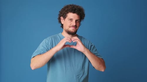 Man Makes Heart Shape with Hands on Blue