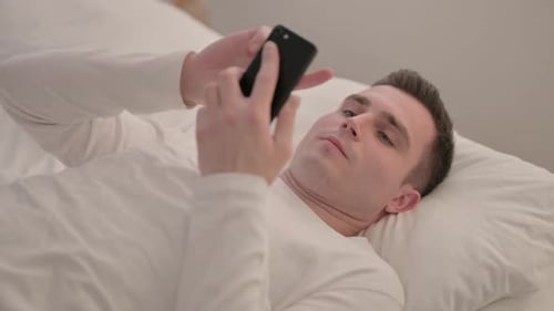 Young Adult Using Smartphone While Lying in Bed