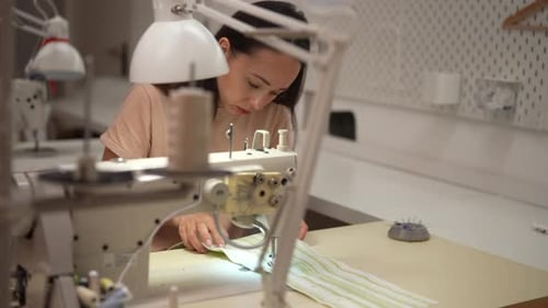 Focused Seamstress Stitching Striped Fabric on Sewing Machine in Workshop Demonstrating Precision
