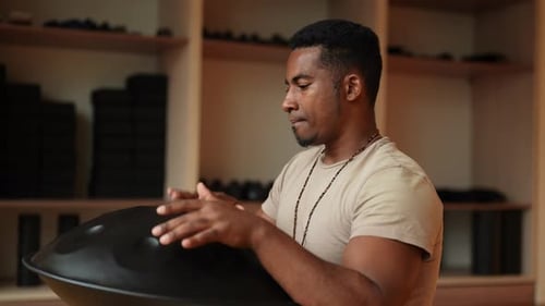 African Young Man in Trance Enjoying Playing By Hands on Glucophone Sitting Crosslegged in Floor at