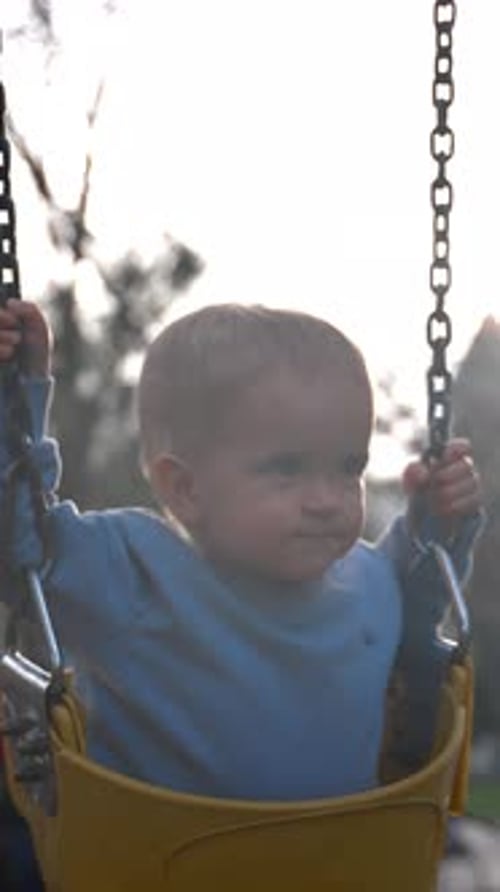 Vertical of Toddler Rides Chain Swings Enjoying Sunny Day in City Park